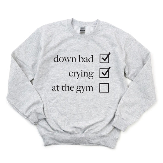 The Not at the Gym • Ash Pullover is a light gray cotton/polyester unisex sweatshirt with down bad and crying marked and at the gym unmarked in black text on the front.