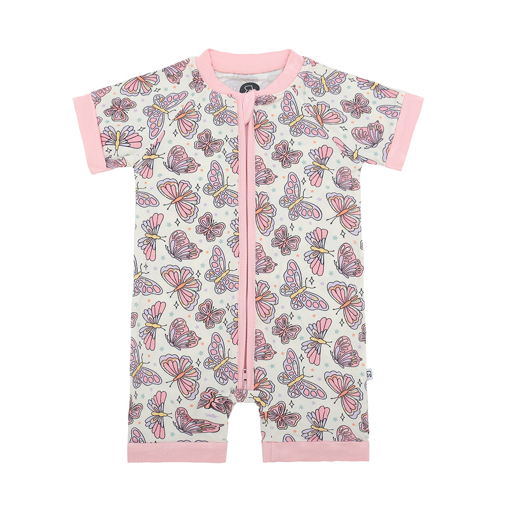 The Flutter By • Bamboo Shorty (Classic Fit) is a cozy, short-sleeved baby romper with pink trim, a front zipper, and a colorful butterfly print on white, made from soft bamboo viscose.