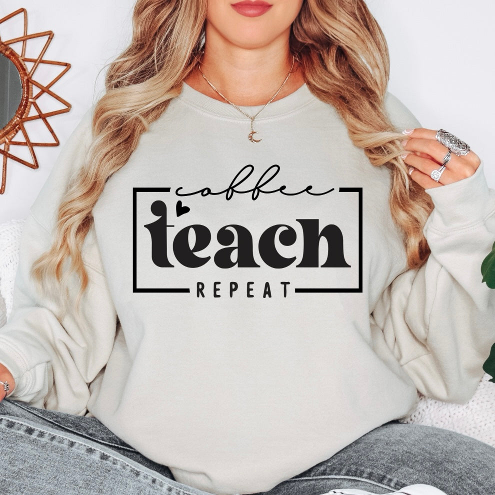 A woman sits wearing the Coffee Teach Repeat • Sand Pullover, a light-colored unisex sweatshirt with “coffee teach repeat” boldly printed on the front, holding the sides of this cozy teacher education top.