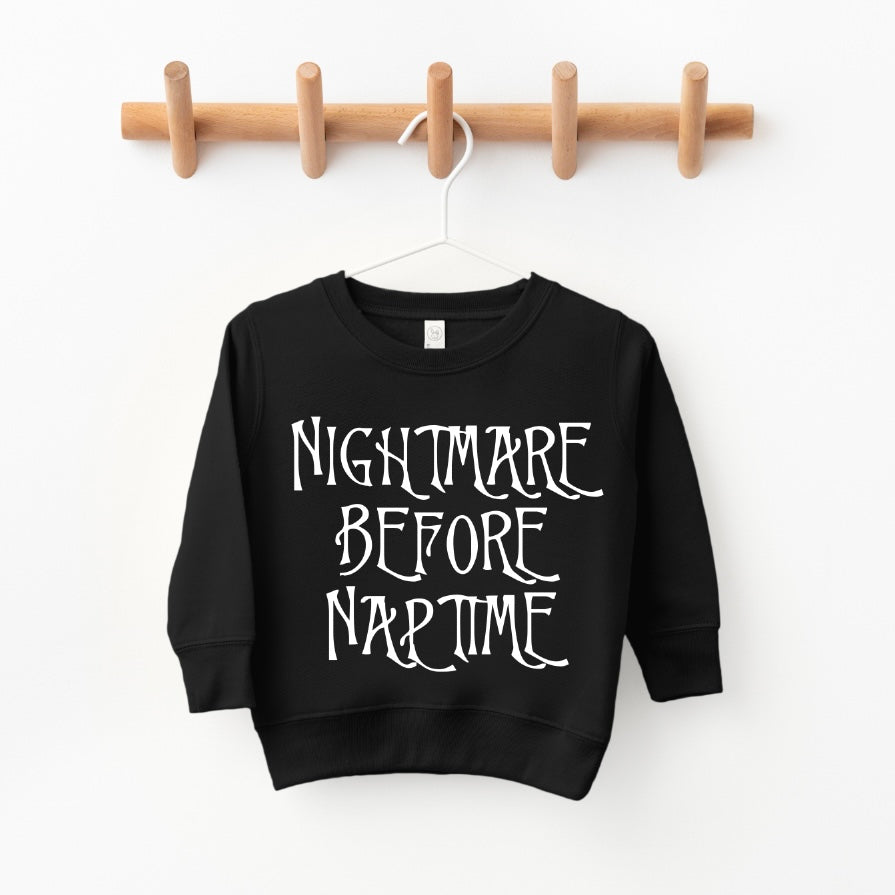 The Nightmare Before Naptime • Kids Pullover is a black, oversized unisex toddler sweatshirt with white spooky text, hanging on a wooden peg rack.