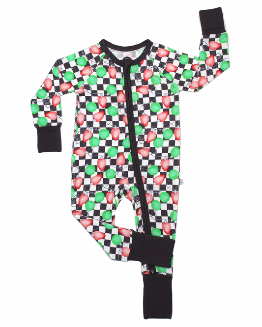 The Checkered Lights • Bamboo Zippy (Updated Fit) is a children’s one-piece pajama featuring black cuffs, a zipper, and a green and red mushroom checkered print inspired by video games. Crafted from soft bamboo fabric, with one arm and leg raised.