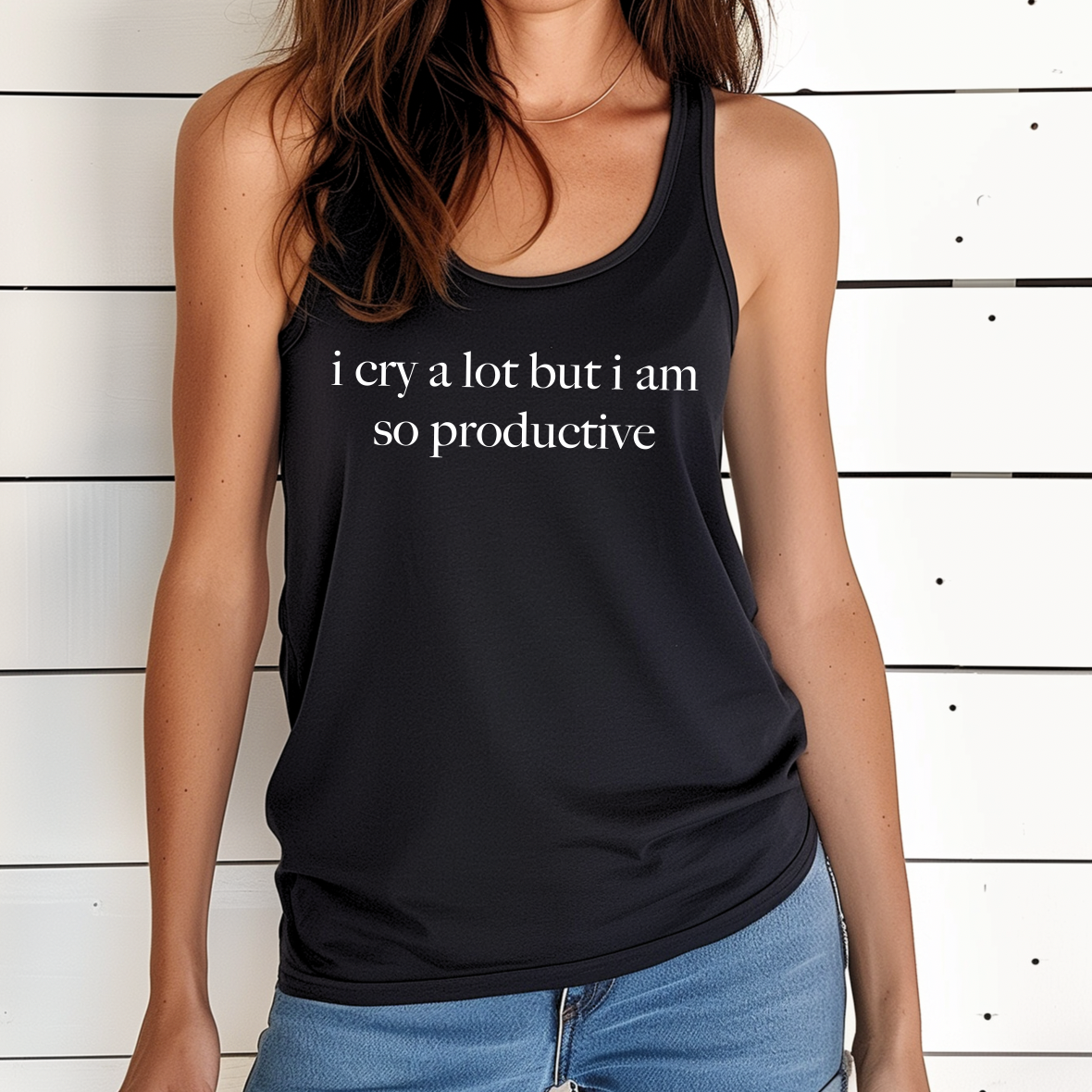 A woman models the i cry a lot Black Tank, featuring a flattering womens racerback fit. She stands against a white wooden wall, with only her upper body visible.