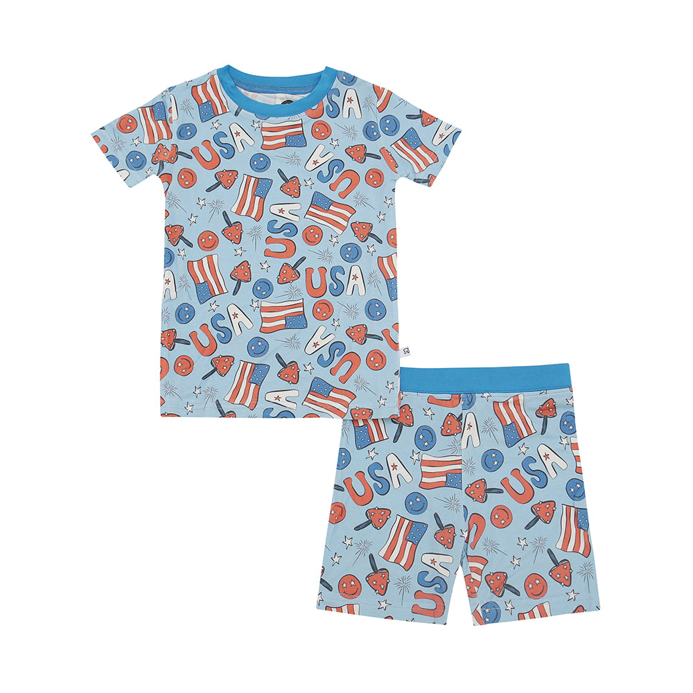 The Stars & Shrooms • Short Sleeve Set (Classic Fit) features a light blue background, stretchy fabric, USA-themed red, white, and blue prints—flags, stars, “USA”—and solid blue collar and waistband for cozy comfort.