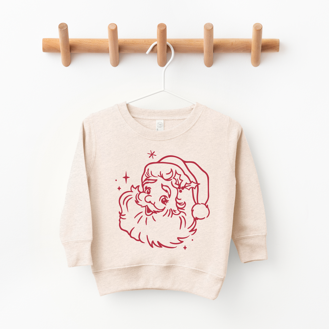 The Vintage Santa Claus • Matching Sweatshirt is a beige unisex kids’ pullover featuring a red line drawing of Santa’s face, shown hanging on a white hanger from a wooden peg rack.