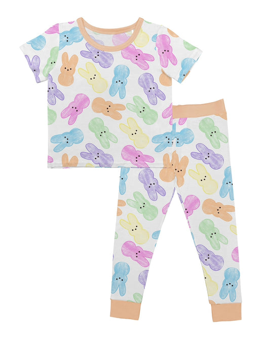 Hoppy Dreams • 2 Piece Bamboo Set (Updated Fit) features a children’s pajama set with short sleeves, long pants, soft bamboo viscose, colorful pastel bunny faces, and beige trim on the collar, cuffs, and ankles.