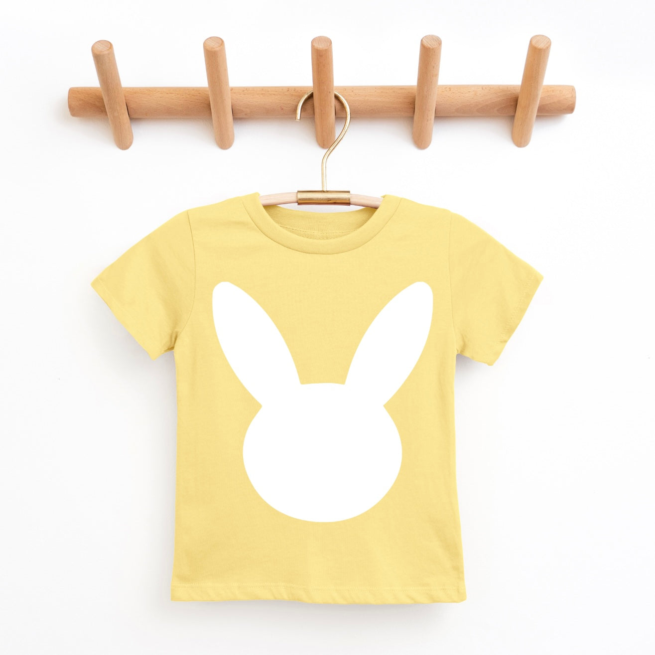 The NEW! Bunny • Butter Yellow Tee is a unisex yellow t-shirt featuring a large white minimalist Bunny design on the front, displayed on a wooden hanger and rack against a white background.