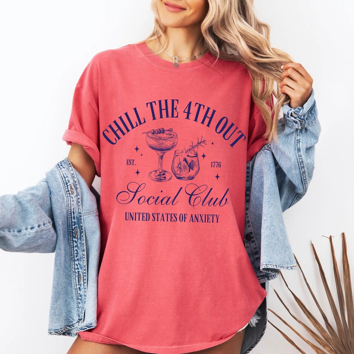 A woman wears the Chill the 4th Out • Comfort Colors Tee, an oversized pink shirt with cocktail sketches and “CHILL THE 4TH OUT Social Club UNITED STATES OF ANXIETY,” styled with a denim jacket over her shoulders.