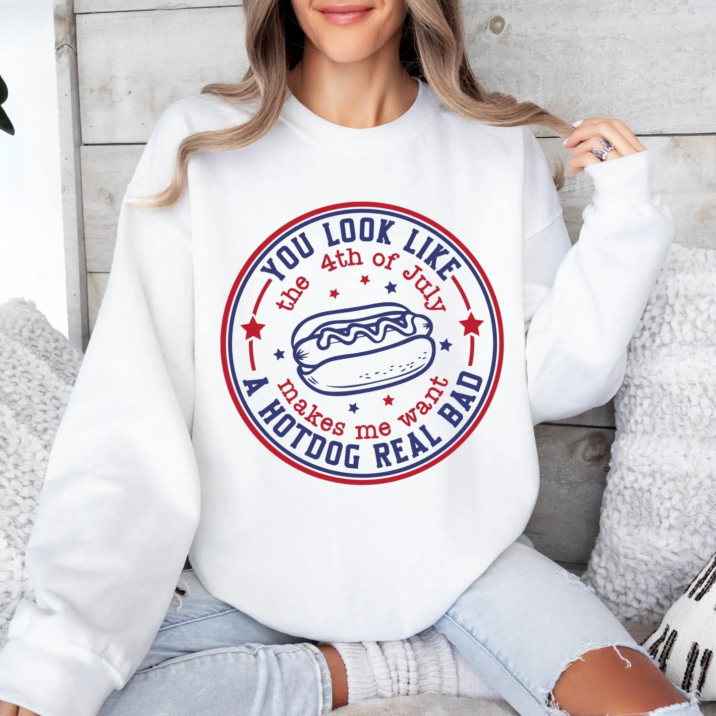 A woman sits cross-legged in the 4th of July • White Pullover, featuring a round hot dog graphic and the text You look like the 4th of July makes me want a hotdog real bad, surrounded by red and blue stars.