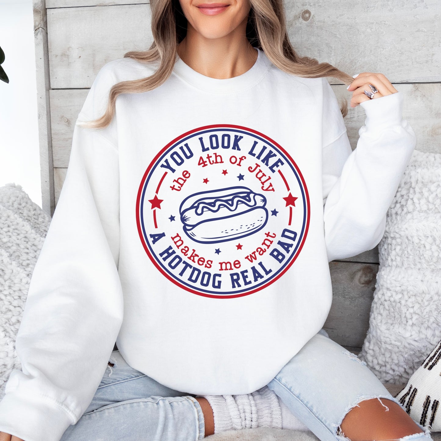 A woman sits cross-legged in the 4th of July • White Pullover, featuring a round hot dog graphic and the text You look like the 4th of July makes me want a hotdog real bad, surrounded by red and blue stars.