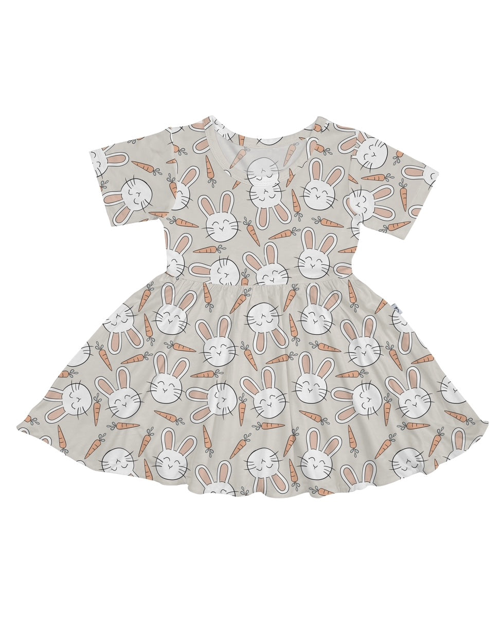 The Snuggle Bunny • Twirl Dress is a short-sleeved, flared dress made from soft bamboo viscose with white bunny faces and orange carrots on a light beige background.