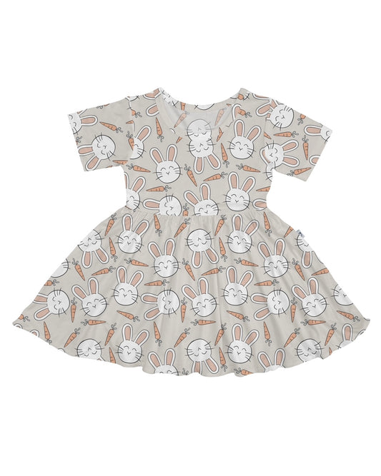 The Snuggle Bunny • Twirl Dress is a short-sleeved, flared dress made from soft bamboo viscose with white bunny faces and orange carrots on a light beige background.