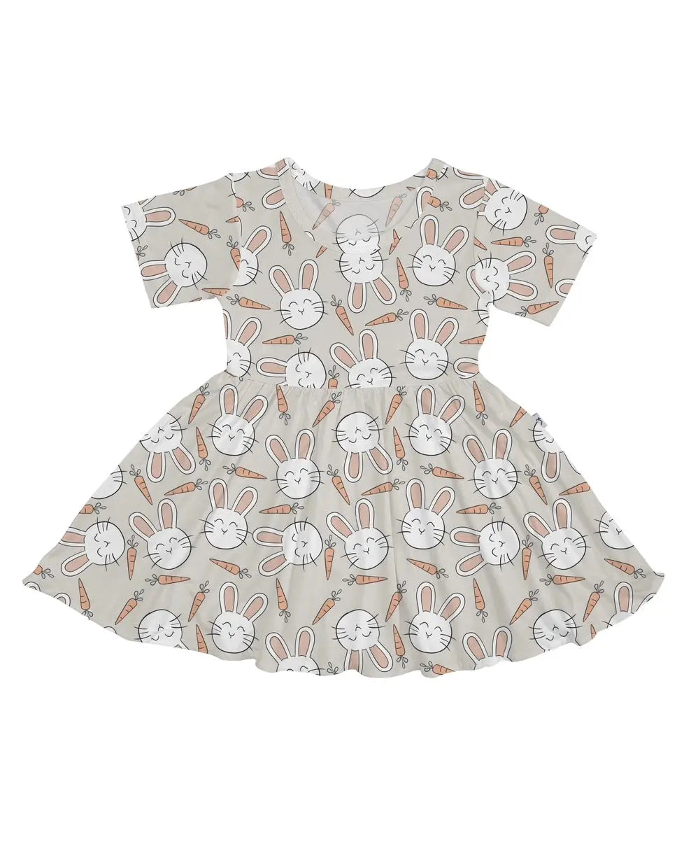 The Snuggle Bunny • Twirl Dress is a short-sleeved, flared dress made from soft bamboo viscose with white bunny faces and orange carrots on a light beige background.