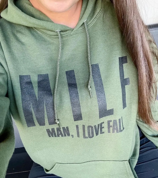 A person wearing the unisex MILF • Olive Hoodie, featuring large black MILF letters and smaller Man, I Love Fall text. Only the lower half of their face and upper body are shown, highlighting this cozy fall sweatshirt.