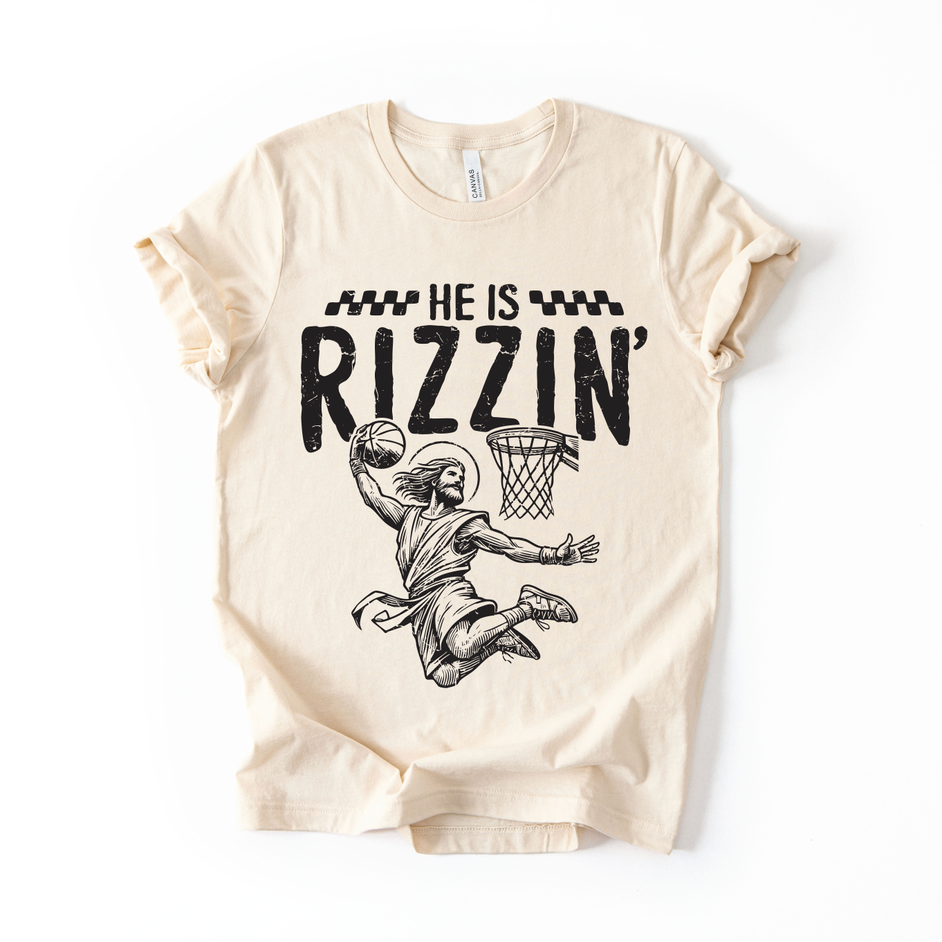 The He is Rizzin • Adult Natural Tee features a soft Airlume cotton build in beige, with a black graphic of a basketball player dunking and bold HE IS RIZZIN’ text. Available in comfortable unisex sizing.