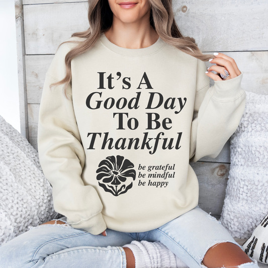 A woman relaxes on a couch, smiling in the Good Day to be Thankful • Sand Pullover—a cozy unisex sweatshirt perfect for enjoying cooler weather and a grateful mindset.