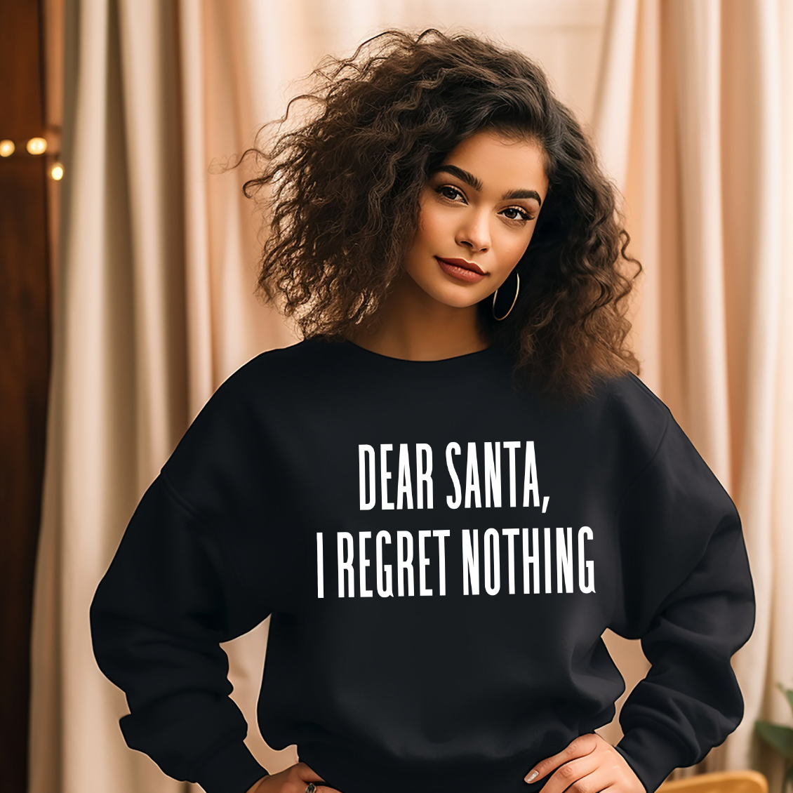 A woman with curly hair and hoop earrings smiles softly at the camera indoors, wearing the I Regret Nothing • Adult Pullover in black. The unisex fit enhances her relaxed, stylish look against a backdrop of curtains.