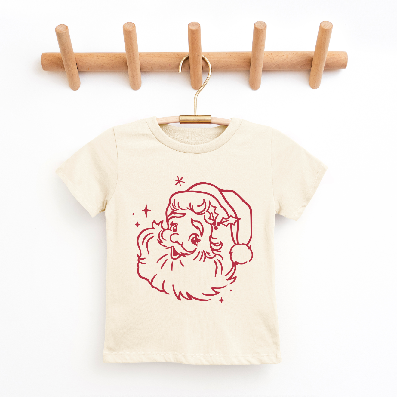 The Vintage Santa Claus • Matching Tee is a cream-colored children’s t-shirt with a red vintage Santa line drawing and stars, crafted on soft Bella/Canvas fabric for a comfy unisex fit. Hangs beautifully on a wooden peg rack.