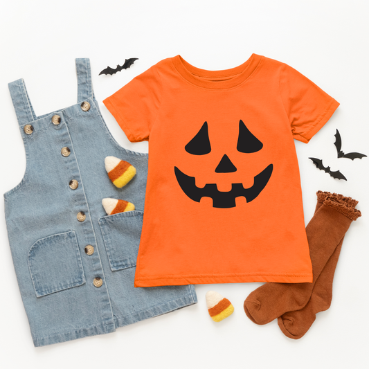 Flat lay of a Halloween outfit with a true to size Jack O Lantern • Kids Tee, denim overall dress, brown socks, felt candy corns, and black paper bats on a white background.