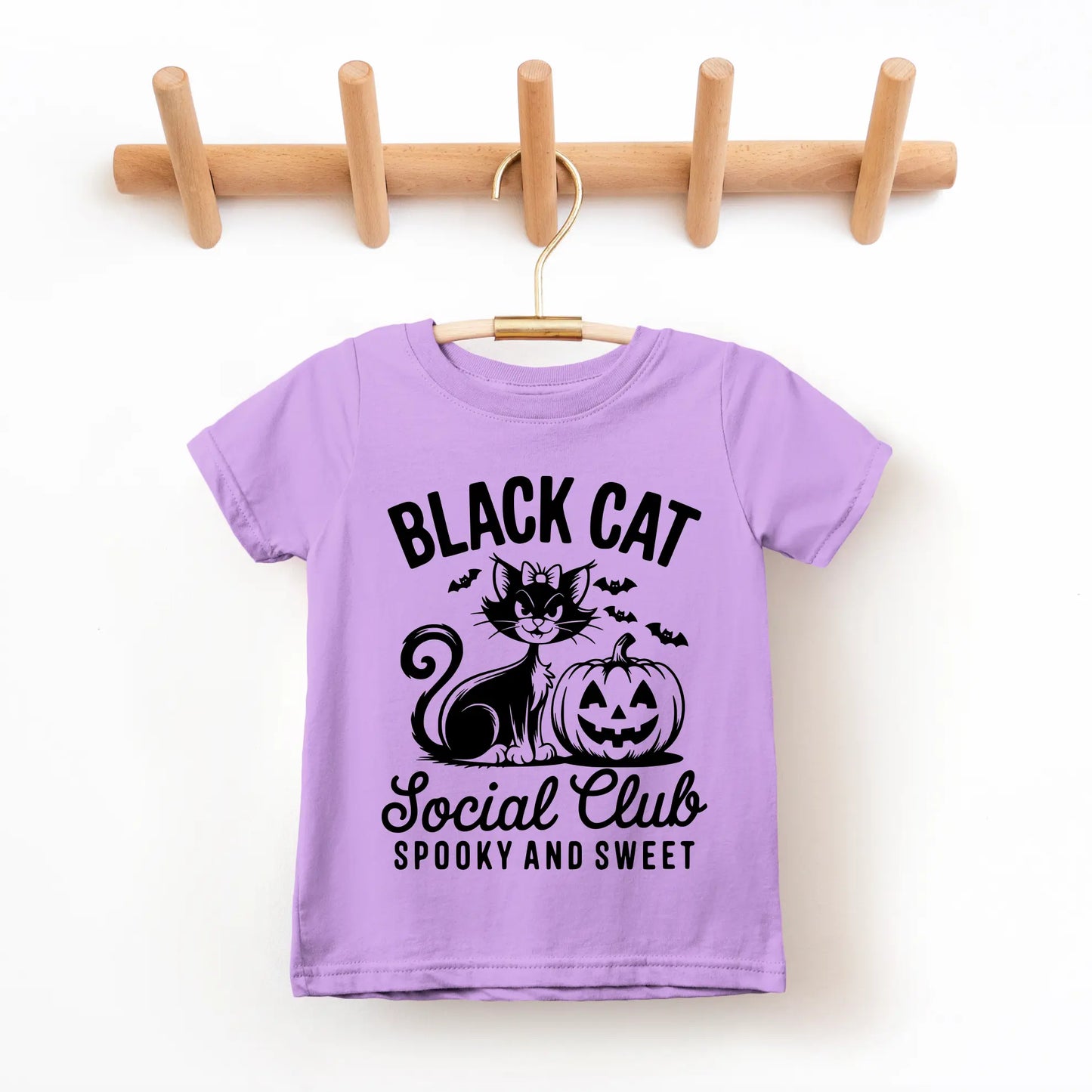 The Black Cat Social Club • Kids Tee is a lavender children’s T-shirt made of soft combed ring-spun cotton. It features a black cat, jack-o’-lantern, bats, and “Black Cat Social Club Spooky and Sweet” in bold black text.