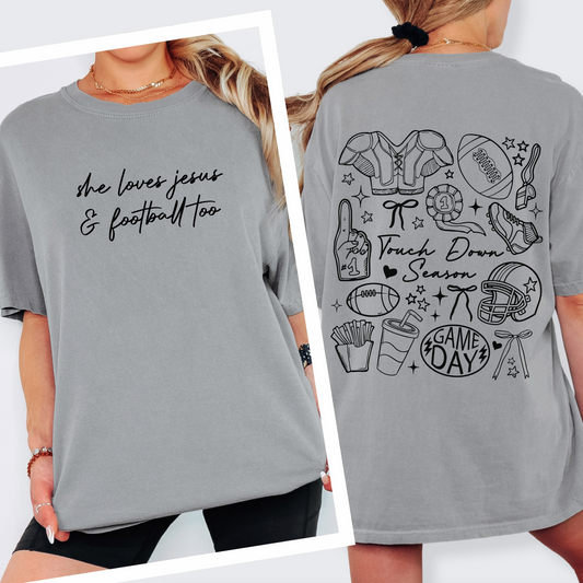 A woman wears the Jesus & Football • Comfort Tee, a soft, gray Comfort Colors shirt with "she loves jesus & football too" on the front and football doodles, gear, snacks, plus phrases like Touch Down Season and GAME DAY on the back.