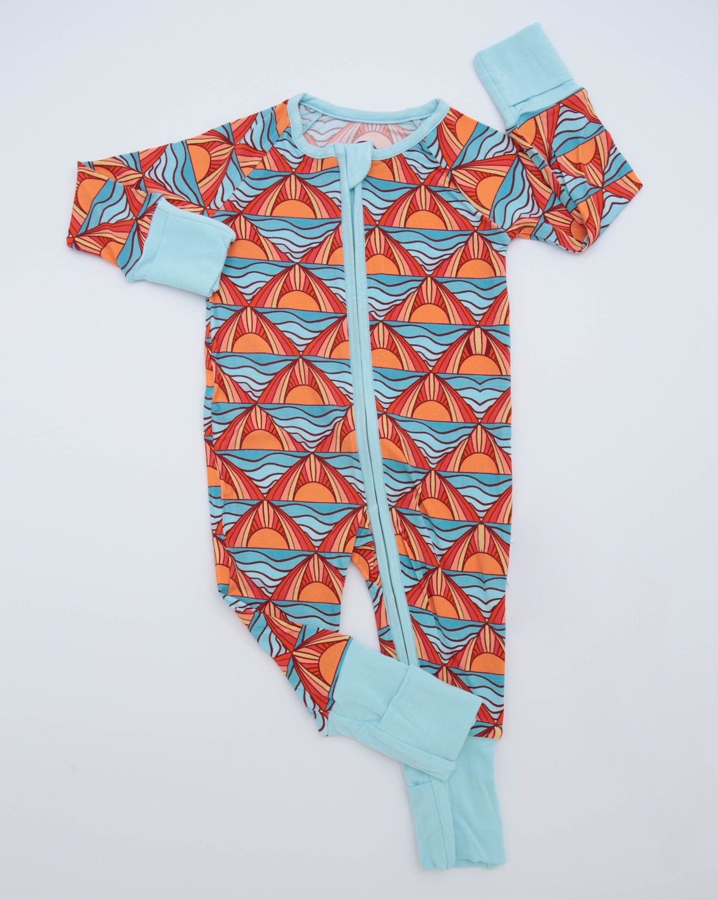 The Maui Sunset • Bamboo Zippy (Classic Fit) is a cozy baby onesie with a zip front, light blue cuffs, and a vibrant orange, red, and blue wave pattern on soft bamboo fabric, shown laid flat on a white background.