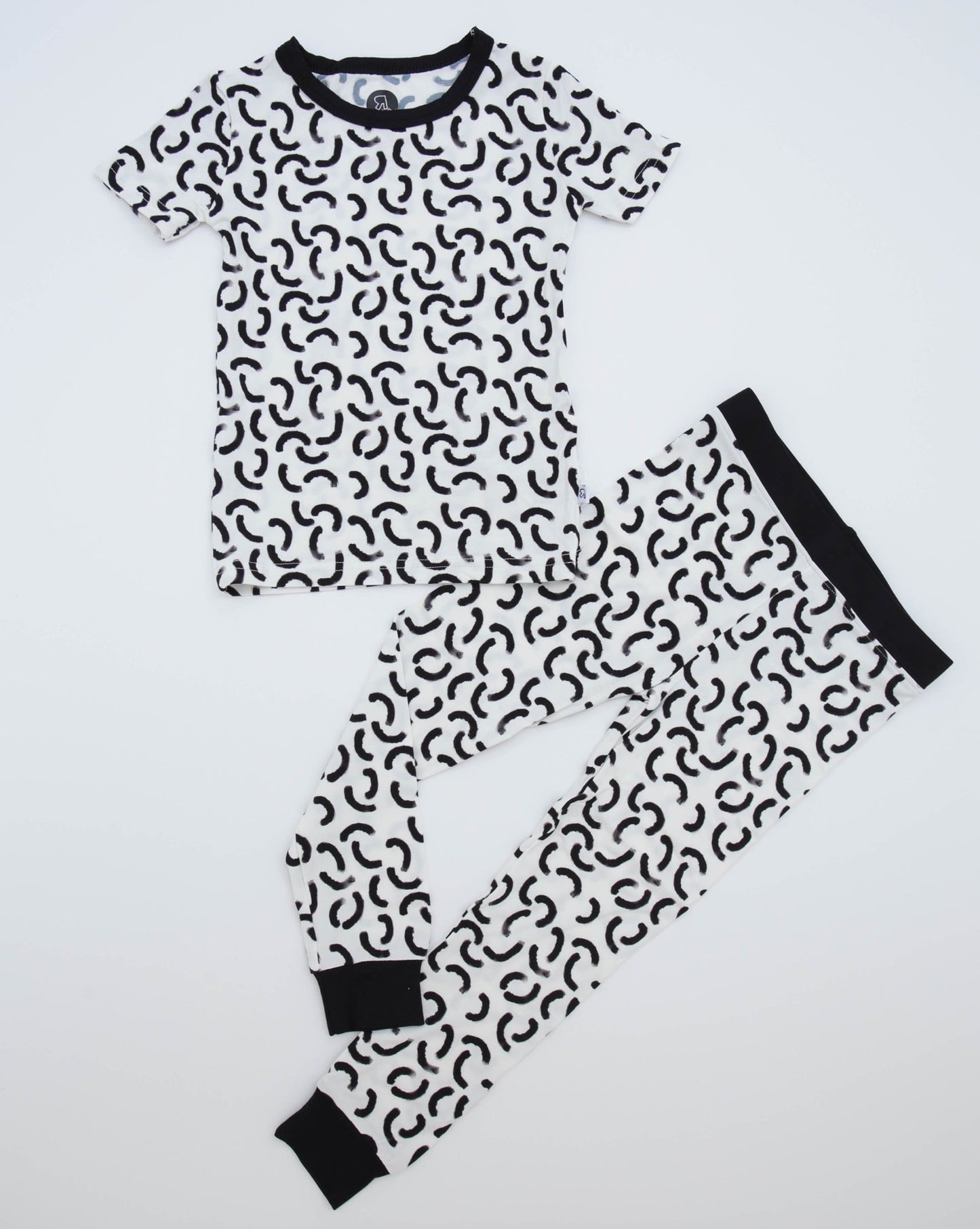 The Monochrome • 2 Piece Bamboo Set (Classic Fit) includes a short-sleeve top and long pants in soft bamboo, with a white background, black abstract squiggles, and solid black cuffs—ideal for eczema-prone skin.