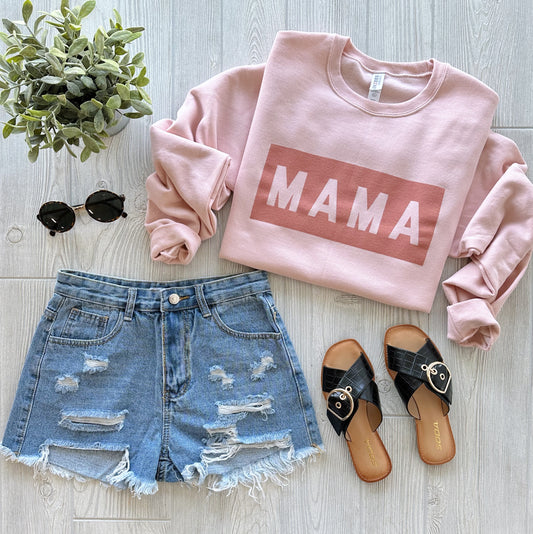 A flat lay of a casual outfit featuring the Mama Matte Rose • Tonal Pullover, distressed denim shorts, black sandals, round sunglasses, and a small potted plant on a light wooden surface.