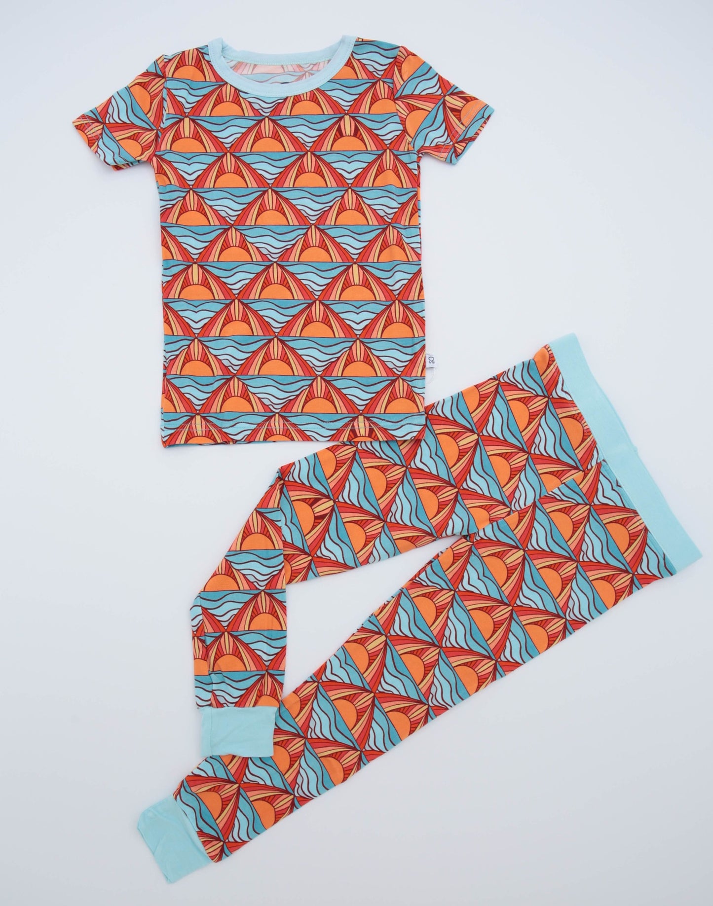 The Maui Sunset • 2 Piece Bamboo Set (Classic Fit) features a short-sleeve shirt and pants with a bold red, blue, and orange geometric pattern and light blue trim—soft bamboo is perfect for sensitive skin; shown laid flat on white.
