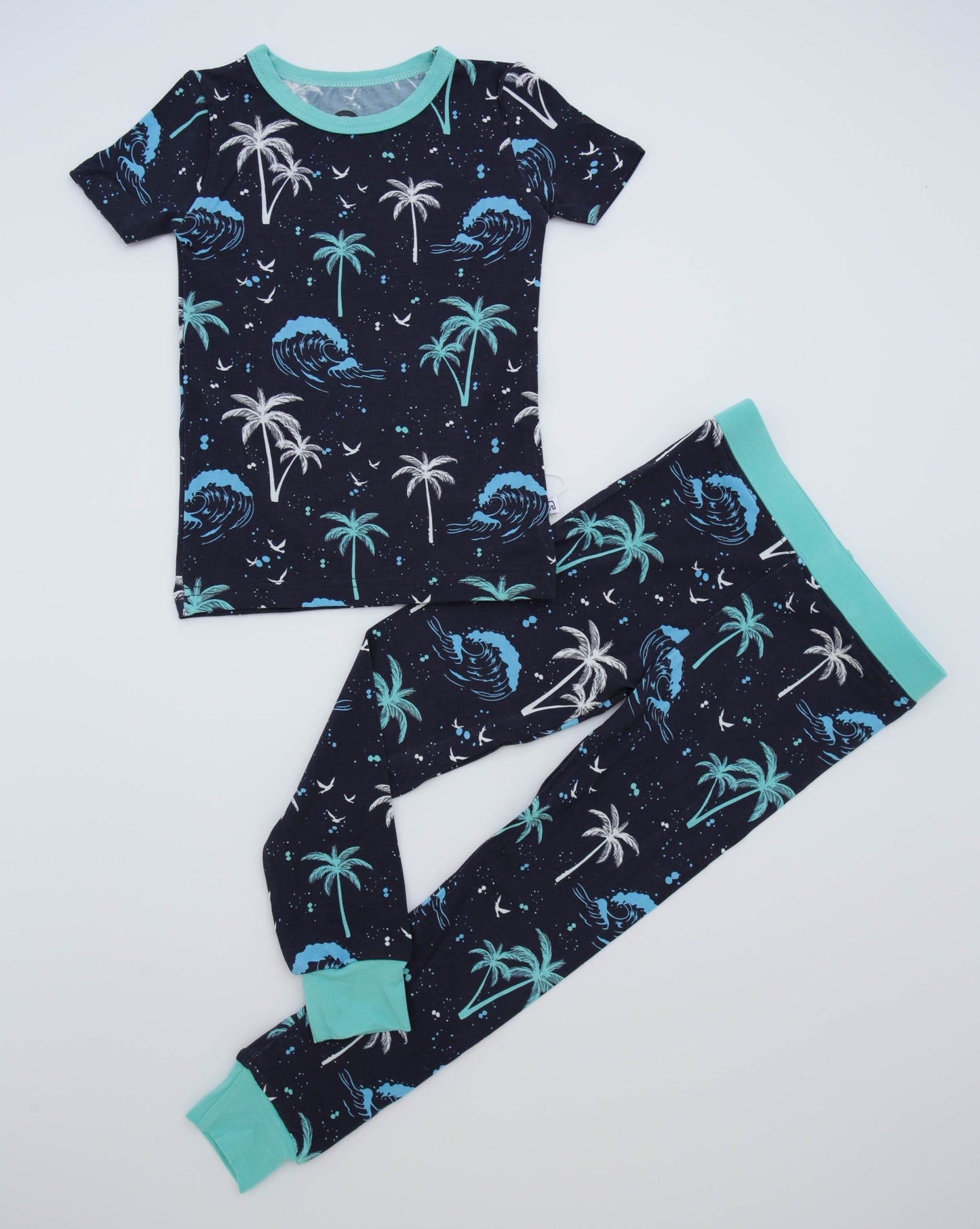 The Surfer Waves • 2 Piece Bamboo Set (Classic Fit) features short sleeves and a cozy blue and white tropical palm tree and wave pattern on a dark background, finished with light blue trim on the collar, cuffs, and waistband.