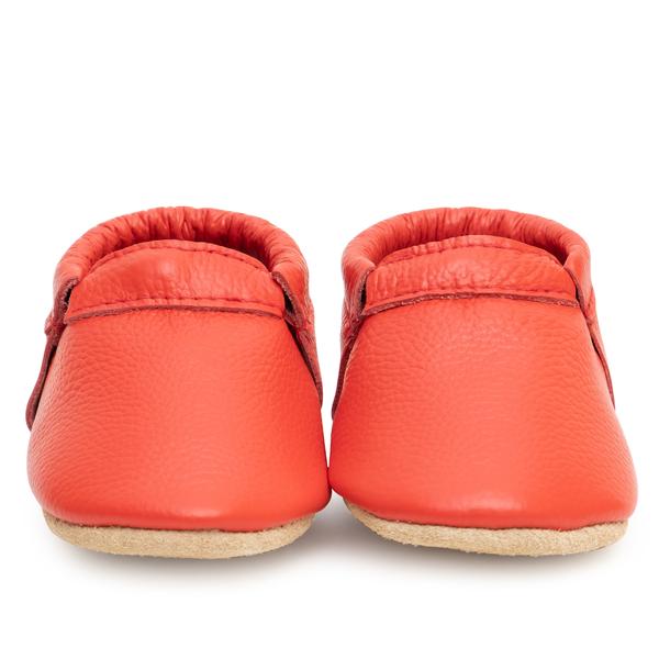 The Red • Fringeless Moccasins are bright red baby moccasins made from genuine leather with soft beige soles, shown front-on against a white background. Check sizing to ensure the perfect fit.