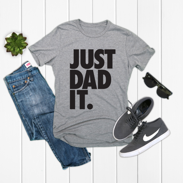 A flat lay of the Just Dad It • Tee in gray—made from soft combed ring-spun cotton—paired with blue jeans, gray Nike sneakers, black sunglasses, and a small potted succulent on a white wooden background.