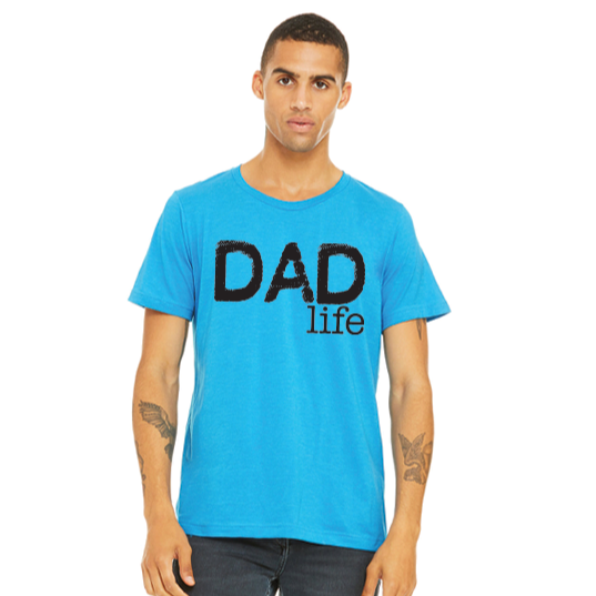 A man stands facing forward with a neutral expression, wearing the OG Dad Life • Neon Blue tee. This unisex essential is crafted from soft, combed, and ring-spun cotton for ultimate comfort, with DAD life printed boldly in black.