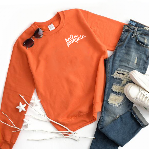 Flat lay of the Hello Pumpkin • Orange Pullover paired with blue ripped jeans, white sneakers, sunglasses, and white decorative branches—a cozy unisex sweatshirt perfect for stylish fall outfits.