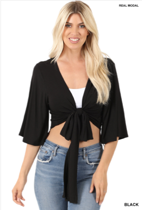 A smiling woman with long blonde hair wears the Jasmine Cardigan in black, styled over a white tank and blue jeans, standing against a plain background. More colors available!.