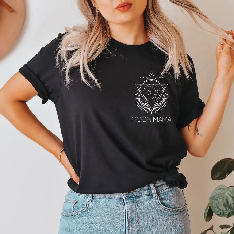 A woman with light hair and red lipstick models the New Moon Mama • Black Tee, featuring a geometric moon and star design. She pairs the unisex-fit shirt, made from soft Airlume cotton, with light blue jeans for a stylish look.