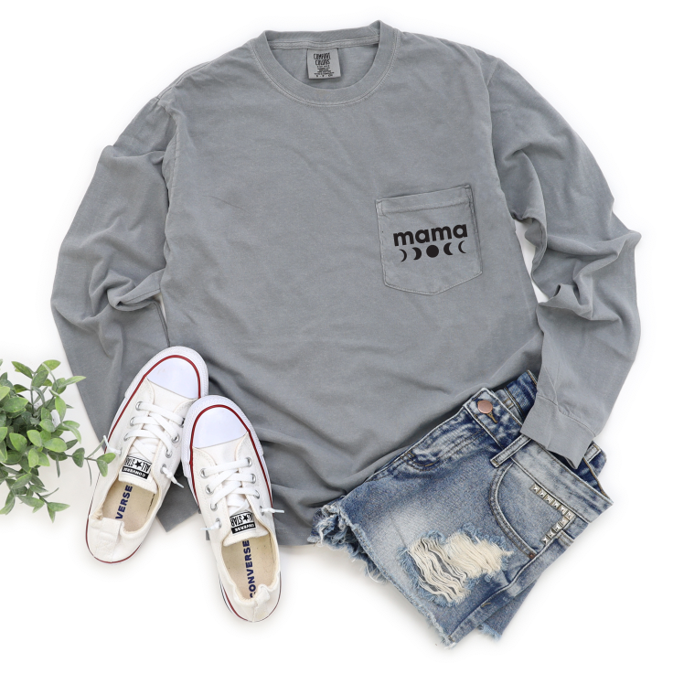 The mama phase • Long Sleeve, a gray vintage-inspired shirt with mama and moon phases on the pocket, is styled with distressed denim shorts, white Converse sneakers, and a small green plant placed beside them.