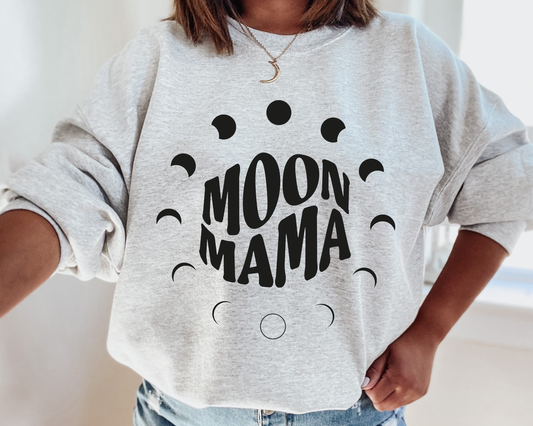 Someone wears the MOON MAMA • Ash Pullover, featuring black moon phase graphics. This cozy unisex sweatshirt is ideal for cooler weather and is shown indoors with the wearer’s face out of frame.