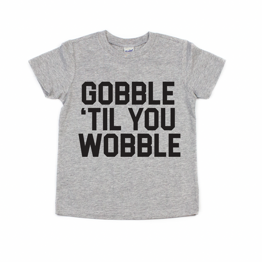 The GOBBLE • Kids Tee is a gray top with bold black GOBBLE TIL YOU WOBBLE text on the front—perfect for a fun, matching look this Thanksgiving.