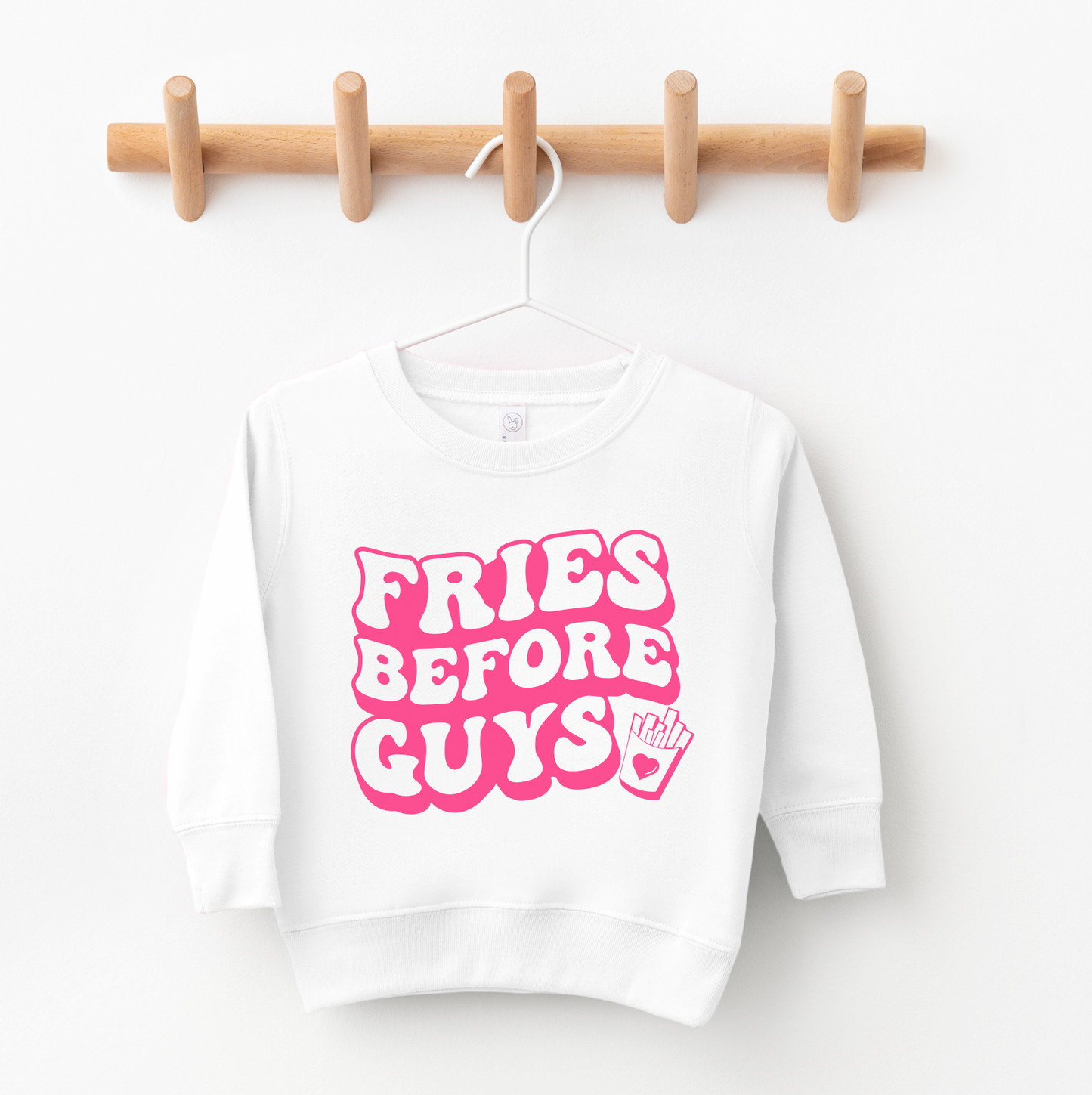 The Fries Before Guys • White Pullover is a unisex sweatshirt on a hanger, featuring bold pink retro lettering and a fries graphic—perfect for kids wardrobes from a small business.