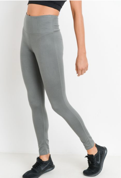 A person wears Basic Sage Leggings • 6168—high-waisted gray poly/spandex leggings with athletic stitch detail—paired with a black crop top and black athletic shoes, standing against a plain white background. The persons head is not visible.