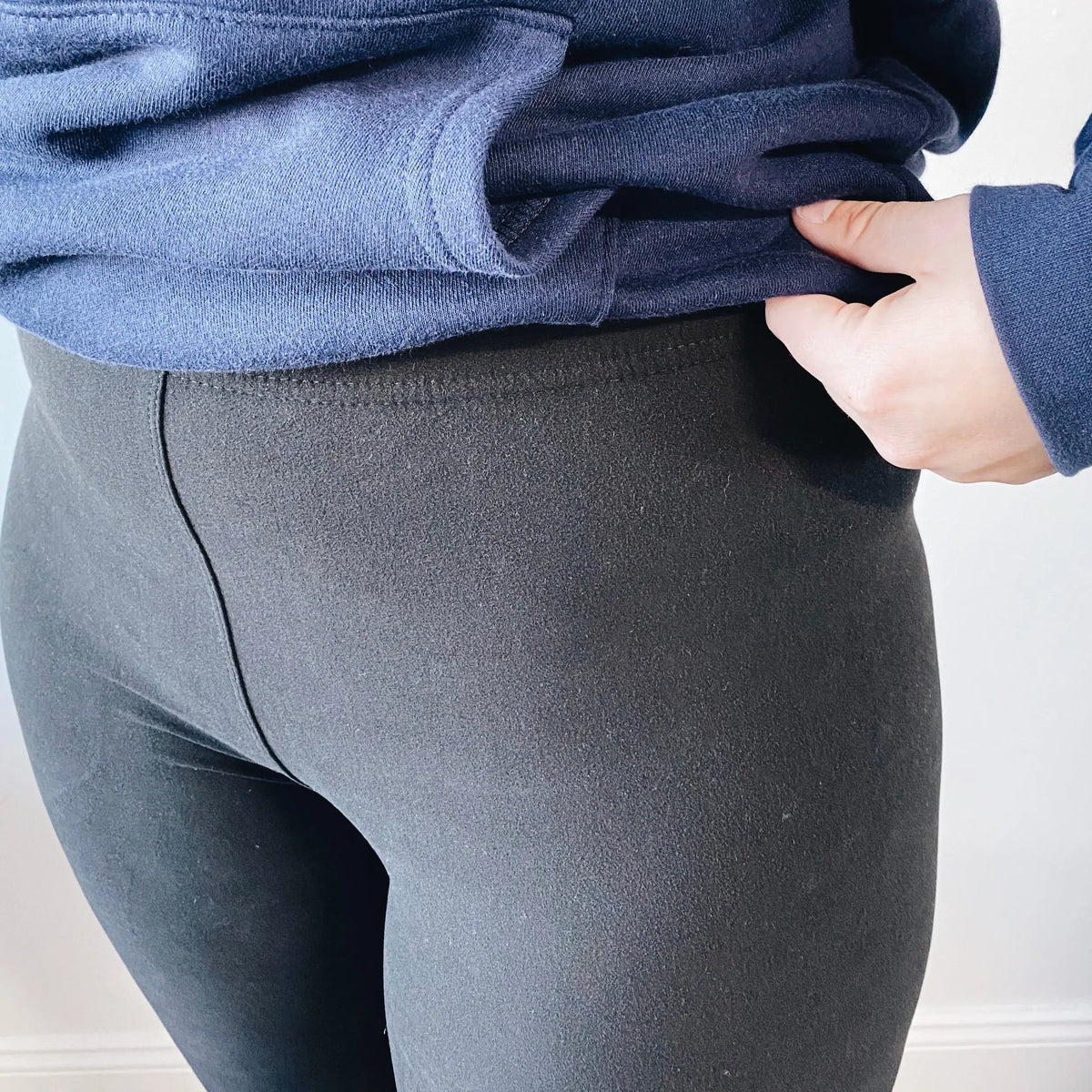 A person is shown from the waist down wearing buttery soft Favorite Leggings (more colors available) and a navy blue sweatshirt, holding up the hem with one hand.