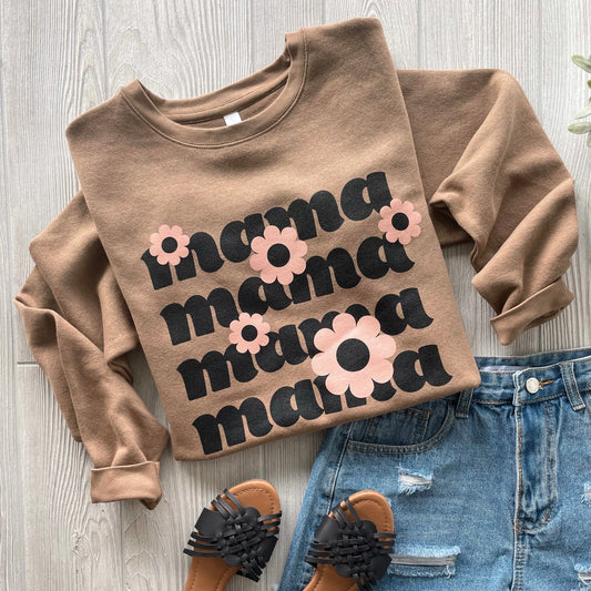 The Daisy Mama • Coyote Pullover, a soft brown combed ringspun cotton sweatshirt with mama in bold black and pink floral details, is styled with denim shorts and black woven sandals on a light wood floor.