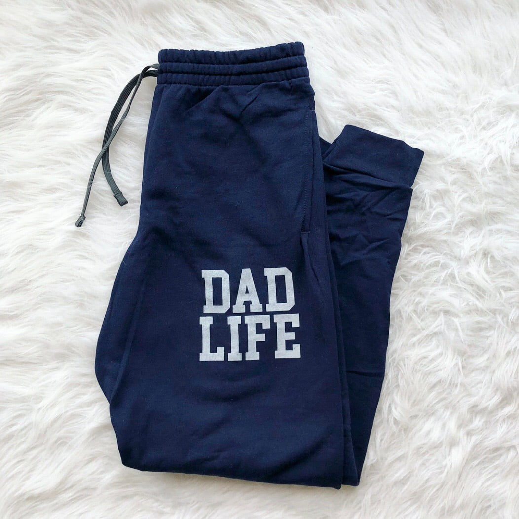 Dad Life Joggers • Navy: Cozy navy blue fleece joggers featuring “DAD LIFE” in bold white letters, shown flat on a soft white background—ideal loungewear for stylish, comfortable relaxation.
