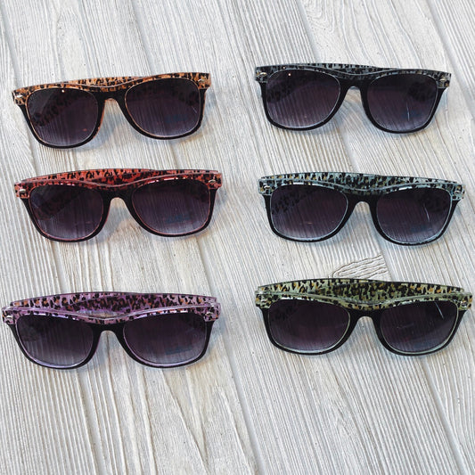 Six Leopard Sunnies • Adult sunglasses with animal print frames and UV400 protection are displayed in two columns on a light wooden surface; each pair features a distinct color, such as red, black, purple, green, and brown.