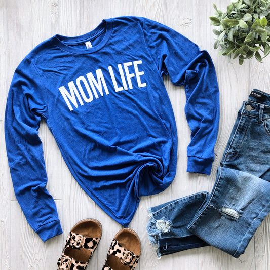 The Mom Life • Royal Blue Long Sleeve is styled with ripped blue jeans, leopard print sandals, and a small green plant on a light wooden floor.
