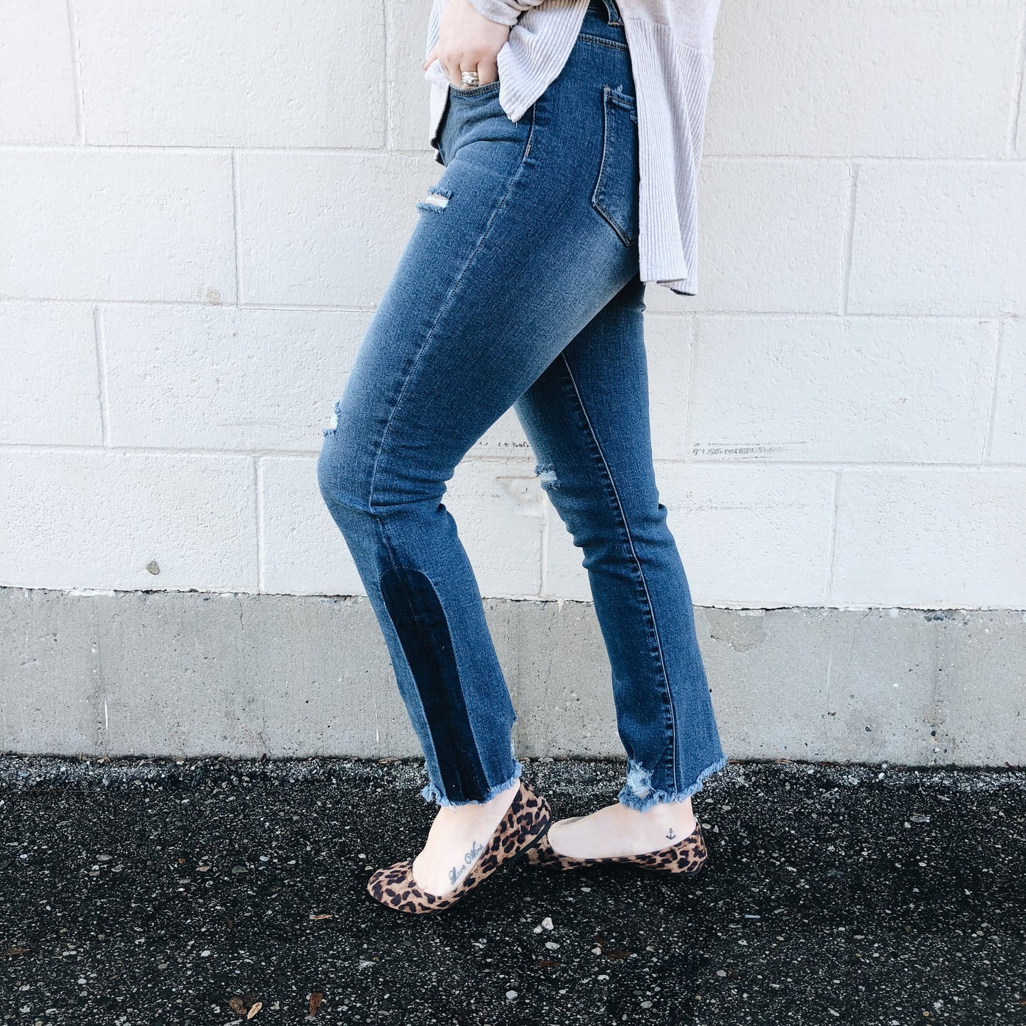 A person stands sideways against a white brick wall, cropped to show only the lower body, wearing Hannah Jeggings SIZE 0 with a dark patch, a light-colored shirt, and leopard print flats.
