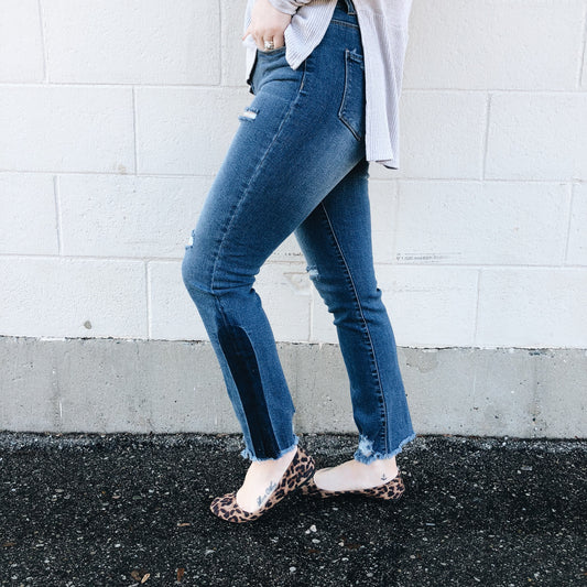 A person stands sideways against a white brick wall, cropped to show only the lower body, wearing Hannah Jeggings SIZE 0 with a dark patch, a light-colored shirt, and leopard print flats.
