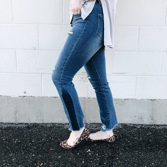 A person stands sideways against a white brick wall, cropped to show only the lower body, wearing Hannah Jeggings SIZE 0 with a dark patch, a light-colored shirt, and leopard print flats.