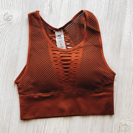 The Grated Sports Bra in brown, size small, features a racerback and front cut-out details. Laid flat on a light wooden surface, it includes a white S-size tag at the neckline and fits true to size. Available in more colors!.