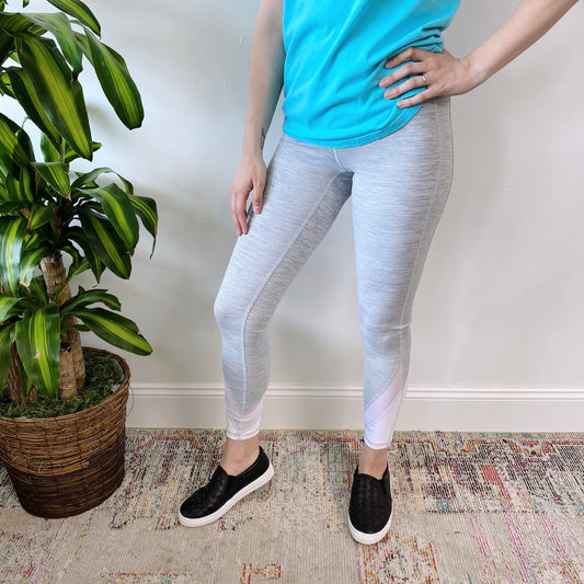 A person wearing a turquoise shirt, Heather Gray Mesh Detail Legging • 2703 SIZE SMALL with side pockets, and black slip-on shoes stands on a patterned rug next to a potted plant, one hand on their hip and head out of frame.